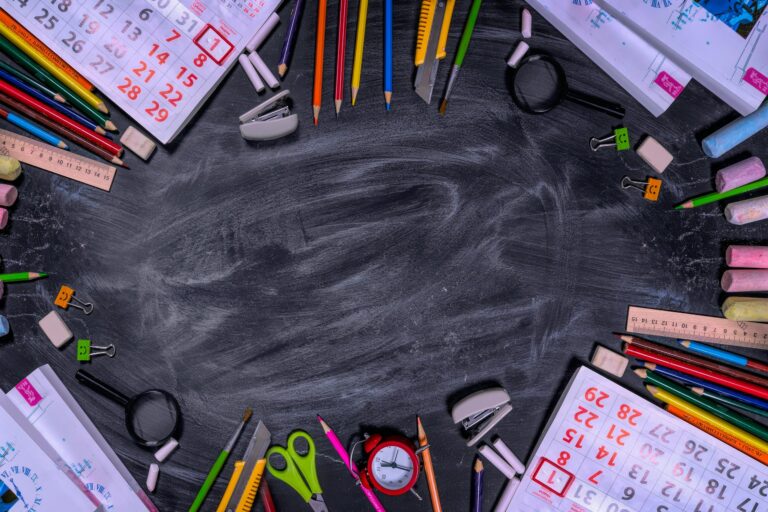 Flat lay of school stationery forming a frame on a blackboard surface.