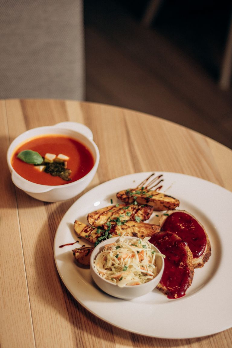 Savory dish with grilled potatoes, meatloaf, cole slaw, and tomato soup on a wooden table.